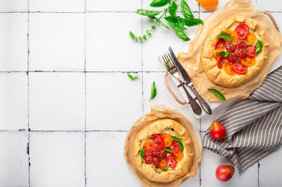 Fresh homemade galettes with tomatoes, ricotta cheese and basil on white tile background. top view.