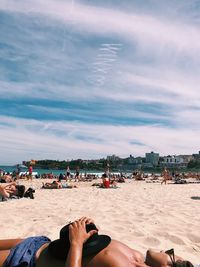 Low section of people relaxing on beach against sky