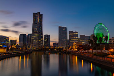 Illuminated buildings by river against sky in city