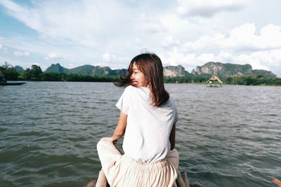 Smiling woman sitting on wooden raft over lake against sky