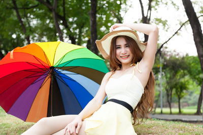 Close-up of young woman wearing hat while sitting on grass field by umbrella