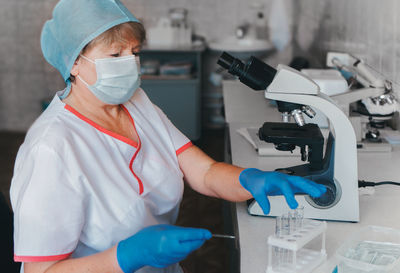 Woman scientist wearing protective gloves, hat and mask working in laboratory making a covid test