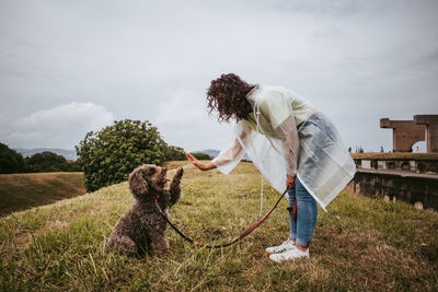 Woman with dog standing on grass against sky