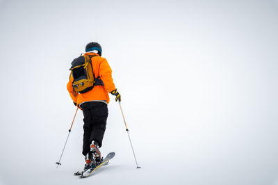 A male athlete in an orange jacket with a backpack on his shoulders and a helmet with a mask in a