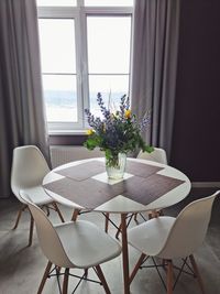 Modern dining room. white table with chairs against window with bouquet of flowers in glass vase