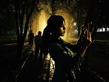 Side view of young woman standing on footpath at night