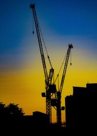 Low angle view of silhouette cranes against sky during sunset