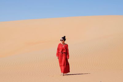 Full length of woman walking on sand dune in desert against clear sky