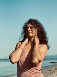 Portrait of smiling young woman standing at beach against sky