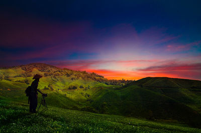 Full length of man photographing while standing on land against sky during sunset