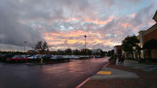 Cars on road in city against sky at sunset