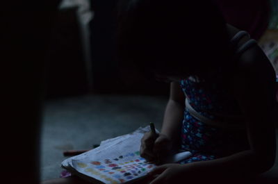 Girl coloring on book while sitting in darkroom