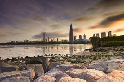 View of buildings by river against cloudy sky