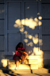 Full length of woman sitting against building