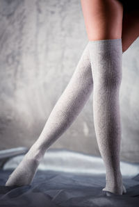 Low section of mid adult woman wearing socks standing on bed at home