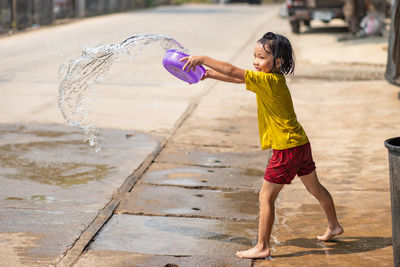 Side view of girl pouring water on road