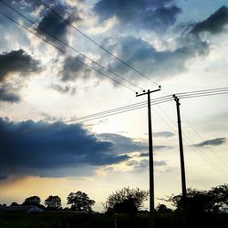 Low angle view of electricity pylon against cloudy sky