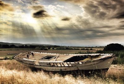 Abandoned boat moored on field against sky