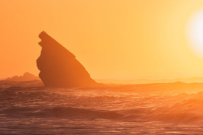 Rock formation in sea against sky during sunset