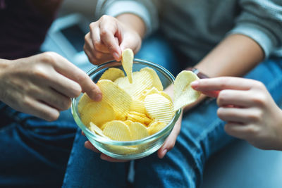 Closeup image of friends sharing and eating potato chips at home party together