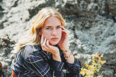 Portrait of young blonde woman in blue dress sitting on stones on background of mountains