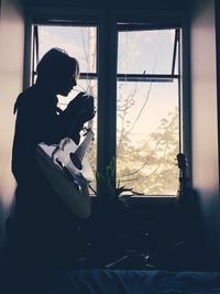 Rear view of silhouette people sitting on window sill