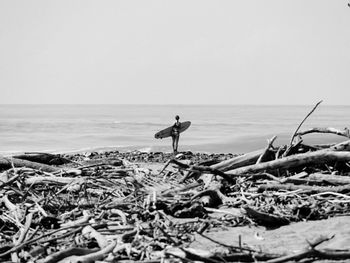 Rear view of woman with surfboard at beach against sky