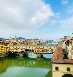 Arch bridge over river amidst buildings in town against sky