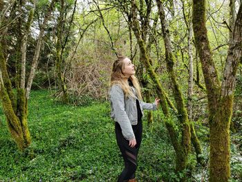 Young woman standing by tree trunk in forest