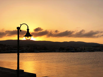 Silhouette street by sea against sky during sunset