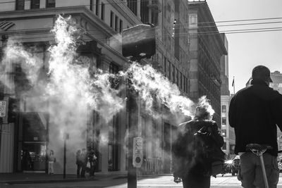 Rear view of people walking by smoke on street in city