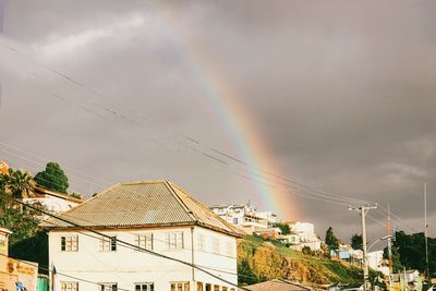 Low angle view of rainbow over houses against cloudy sky