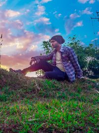 Full length of young woman sitting on field against sky during sunset