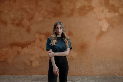 Portrait of young woman standing against wall