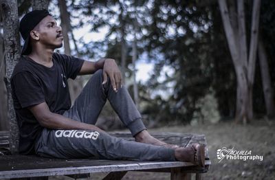 Young man looking away while sitting on tree