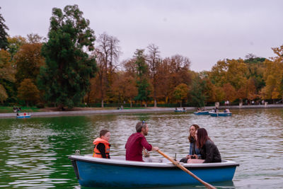 People sitting on boat in lake against trees