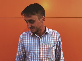 Portrait of young man looking away against orange wall