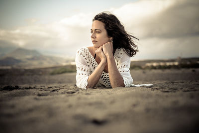 Thoughtful young woman lying on field against sky during sunset