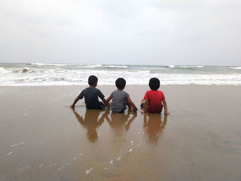 Rear view of children on beach against sky