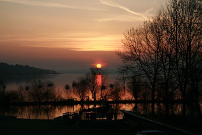 Silhouette bare trees by lake against sky during sunset