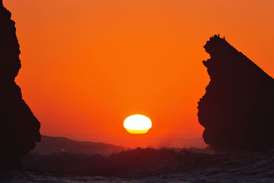 Silhouette rock formation in sea against romantic sky at sunset