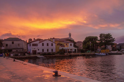 Buildings by lake against sky at sunset