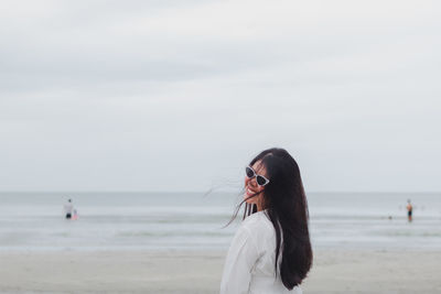 Young woman wearing sunglasses standing on beach against sky