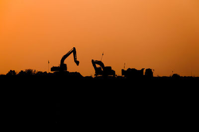 Silhouette people at construction site against orange sky