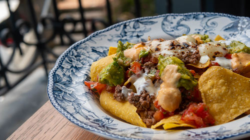 Corn chips nachos with fried minced meat and guacamole on wooden background.