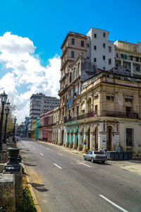 Cars on road by buildings in city against sky