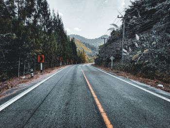 Empty road amidst trees against sky