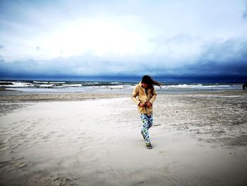 Full length of girl walking at beach against sky