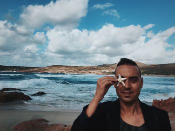 Portrait of man with artificial starfish at beach against sky