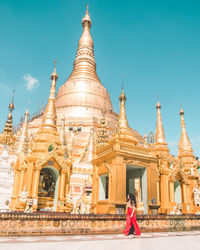 Side view of young woman standing by pagoda against blue sky during sunny day